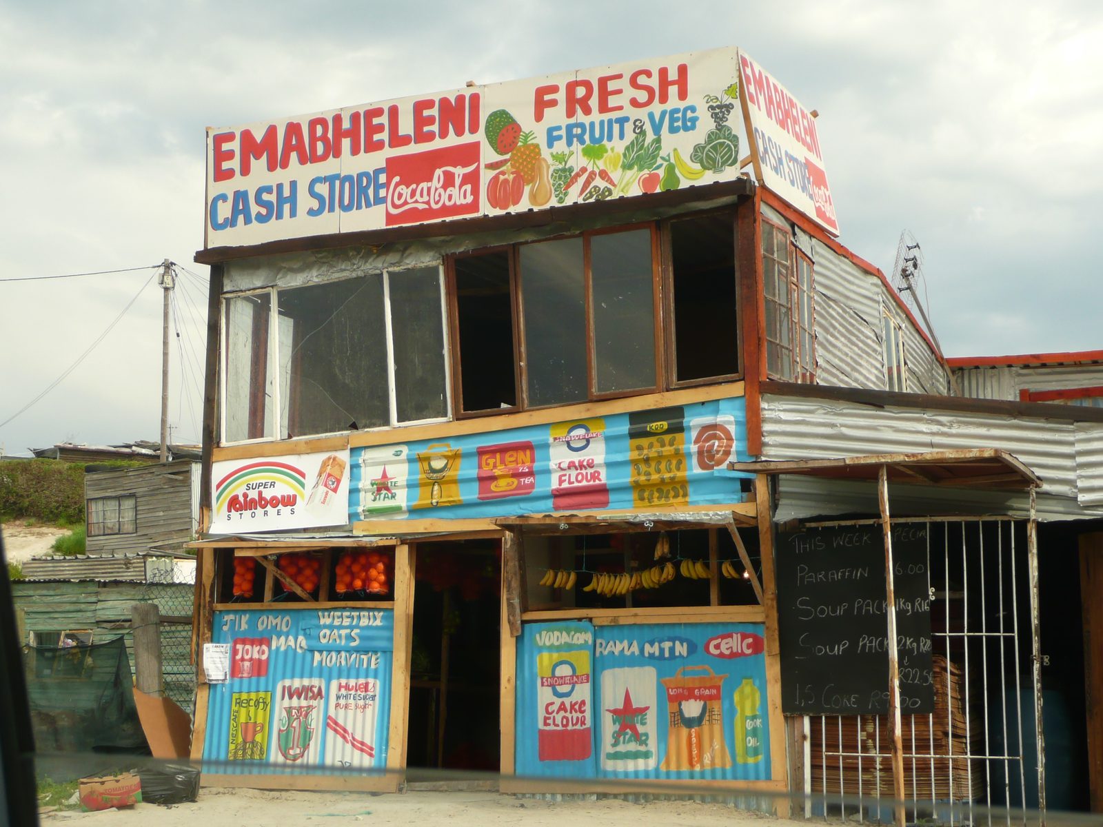 A township cash store and informal retail outlet serving local residents, where micro-traders face escalating wholesale prices and municipal licensing hurdles.